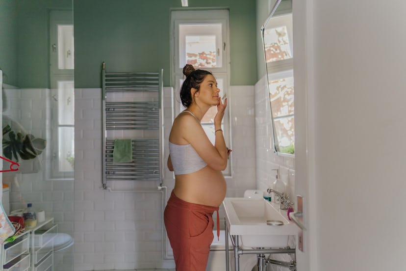 Pregnancy safe skin care is important for this woman, who is pregnant, applying her moisturizer in t...