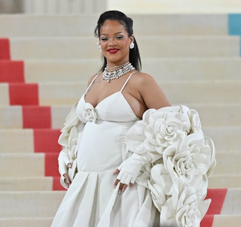 Rihanna wears a sleeveless white gown with a rosette-covered stole at The 2023 Met Gala. 