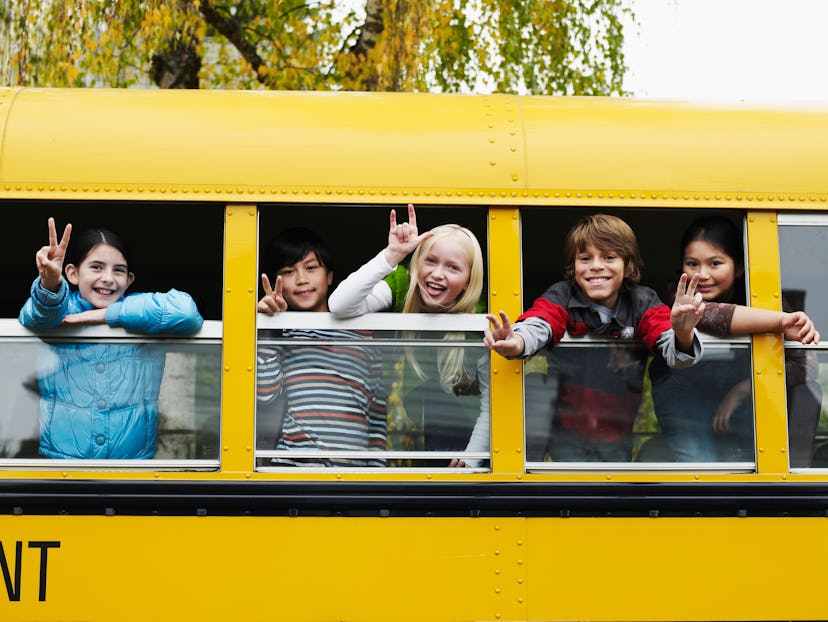 Group of young students hanging out windows of school bus making peace sign in article about back to...