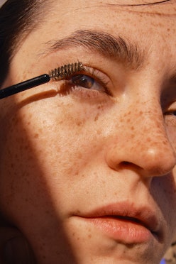 close up of a freckled woman's face brushing her eye lashes