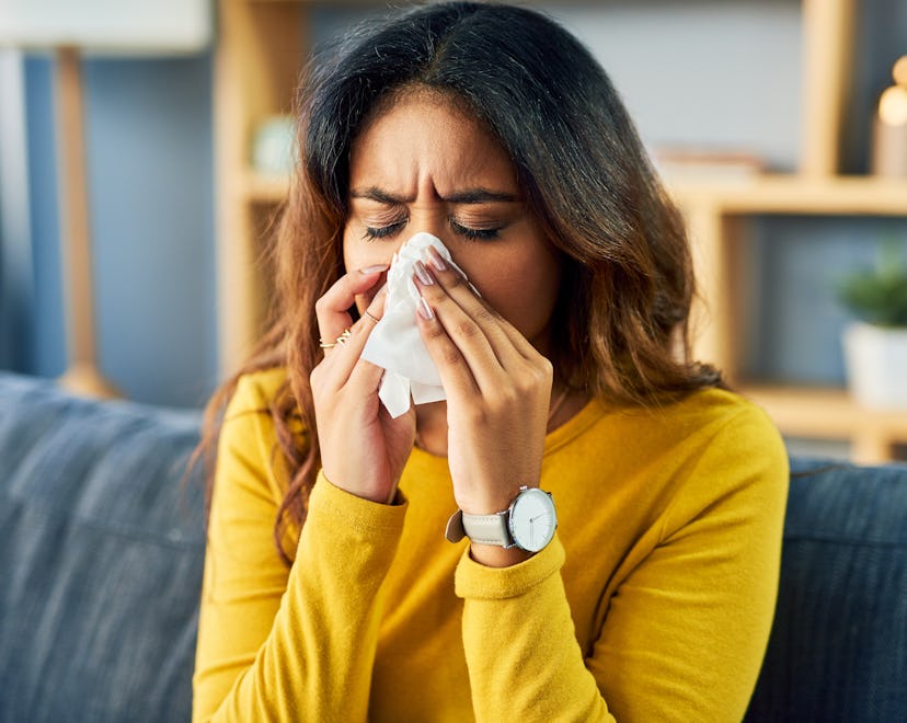 Shot of a young woman blowing her nose while sitting at home, stuffy nose an early sign of pregnancy