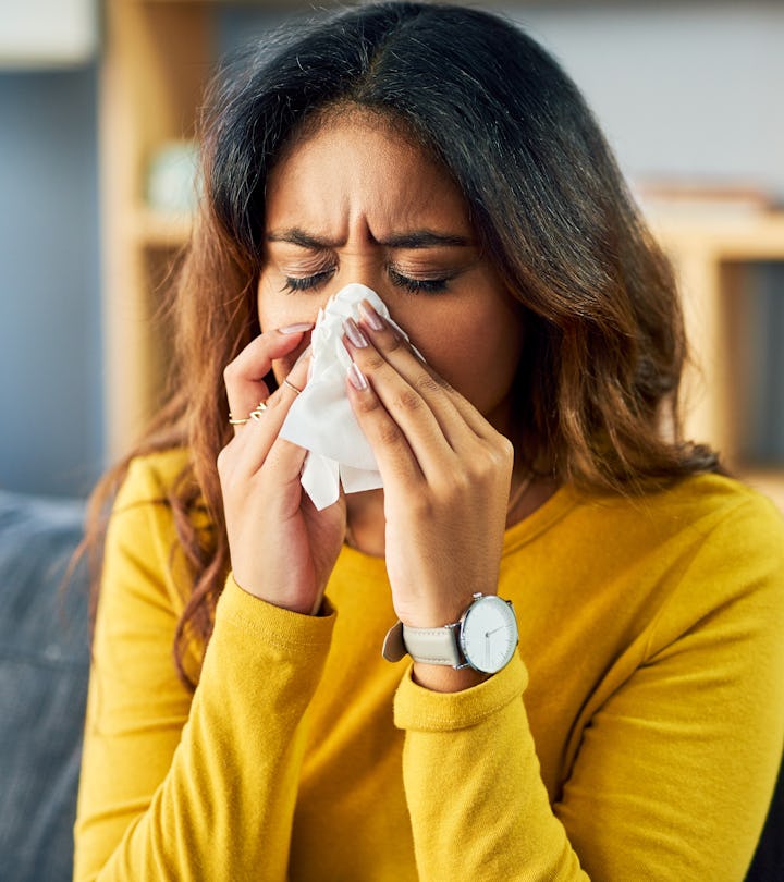 Shot of a young woman blowing her nose while sitting at home, stuffy nose an early sign of pregnancy