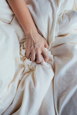 Close up of a woman's hand gripping a bed sheet in article about when its safe to masturbate after a...