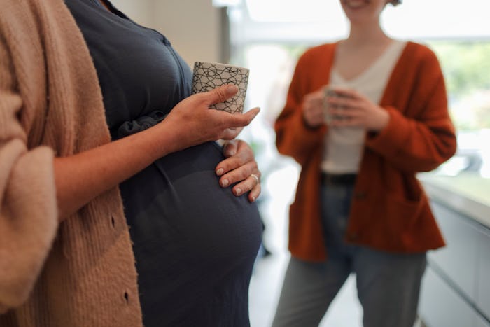Close up cropped pregnant woman and friend drinking tea in domestic kitchen