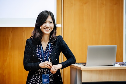 A businesswoman  leaning on a podium and smiling while giving a presentation at a business conferenc...