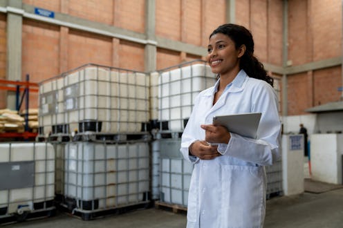 Portrait of a happy Latin American woman working as a supervisor at a chemical plant and holding a t...
