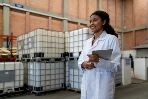 Portrait of a happy Latin American woman working as a supervisor at a chemical plant and holding a t...