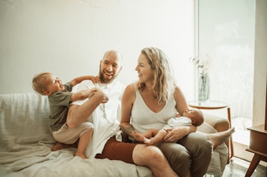 Two parents and their child laughing on the sofa in the living room of their home.