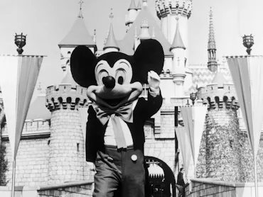 circa 1955: A person in a Mickey Mouse costume at the gate of the Magic Kingdom at the Disneyland t...