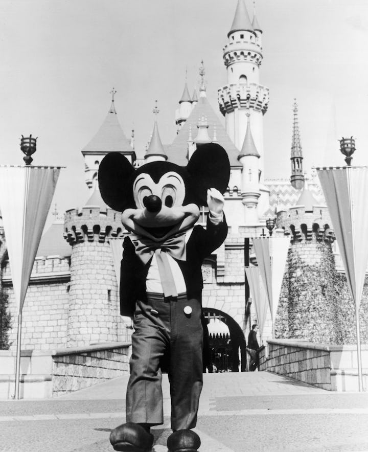 circa 1955: A person in a Mickey Mouse costume at the gate of the Magic Kingdom at the Disneyland t...