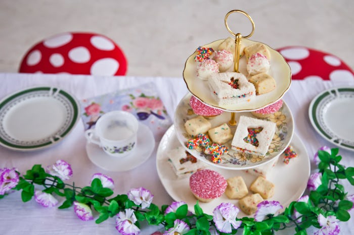Fairy baby shower table spread with tea sandwiches, flower garlands, tea cups, and toadstool seats.
