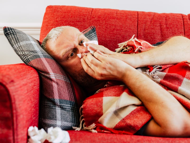 Portrait of a man suffering from hay fever allergy lying on his red sofa at home. He is surrounded b...