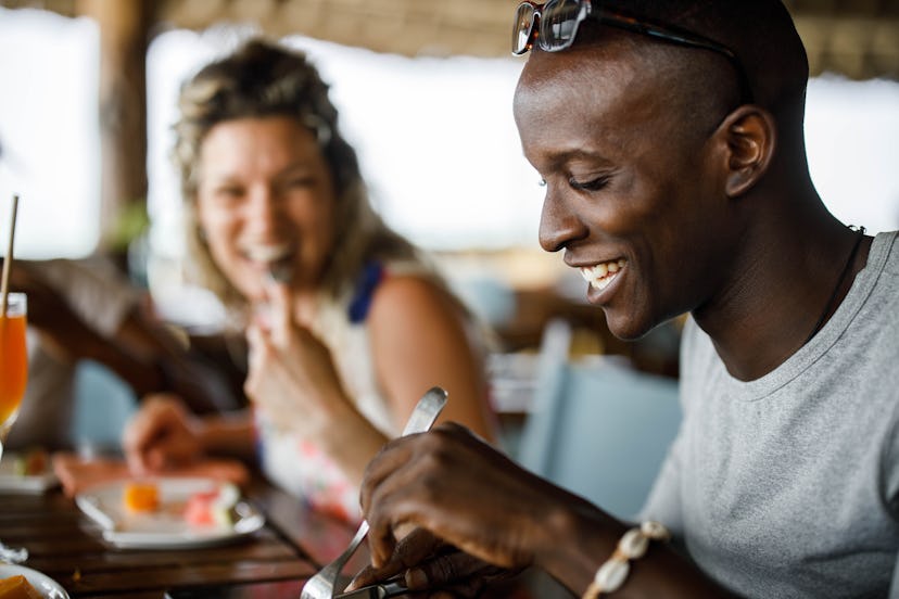 Happy African American man enjoying while having lunch with his friend on a restaurant's terrace.