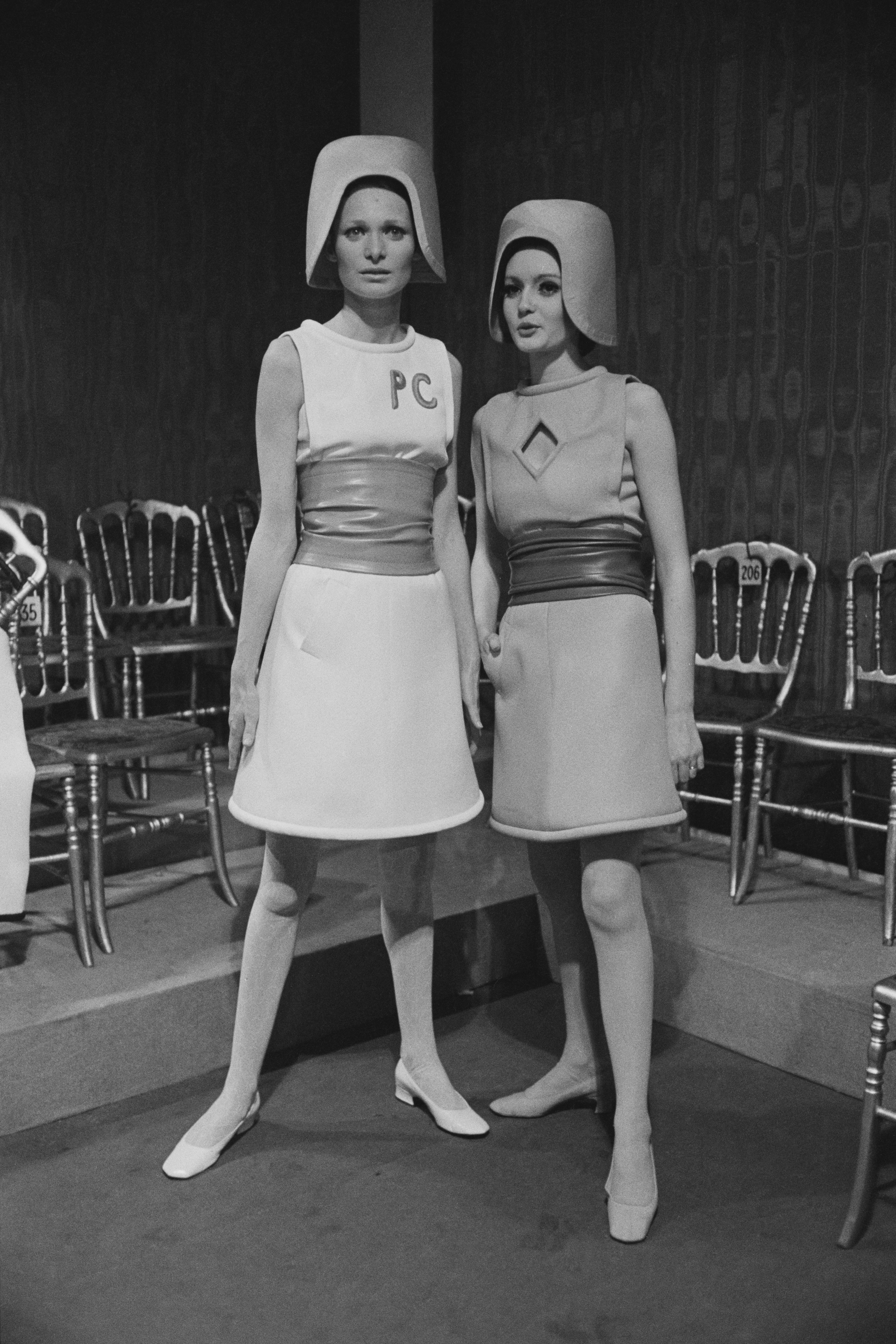 Two fashion models wearing belted wool sleeveless dresses by Pierre Cardin.