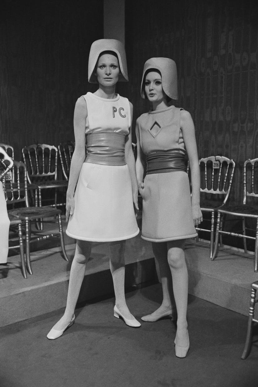 Two fashion models wearing belted wool sleeveless dresses by Pierre Cardin. 