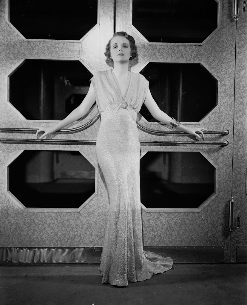 Mary Astor wears a sleeveless gown with a small cut-out above the navel. 