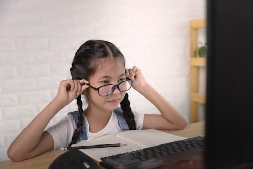 an Asian girl 9 years old wears eyeglasses looking at a laptop. Have sight problem, Learning online ...