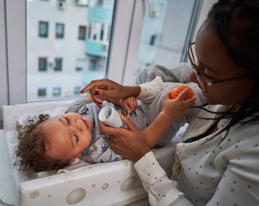 Caring single mother applying baby eczema lotion on her baby boy