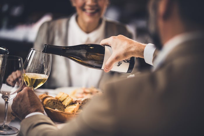 Close up of unrecognizable man pouring wine to his wife during lunch in a restaurant.