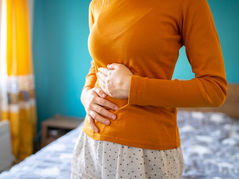 A young woman is having pain in her stomach and holding it with both hands