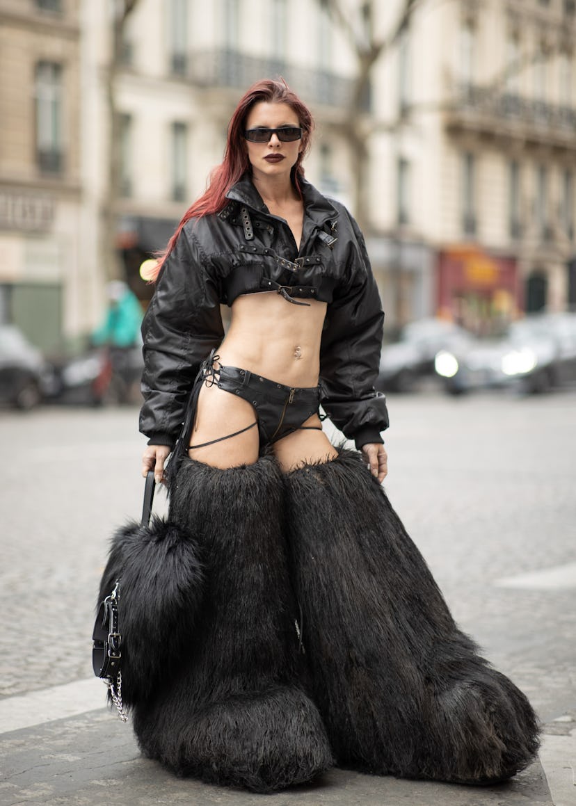 Julia Fox wears a thong, a crop jackets, and massive oversized furry boots. 