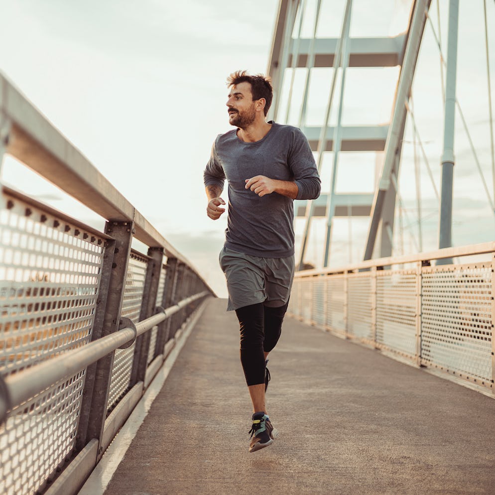 Athletic young man running on a bridge during sunset.