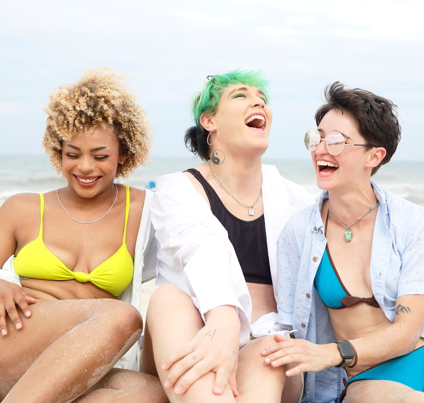 three friends share a laugh on the beach as they consider which zodiac signs will be the luckiest in...
