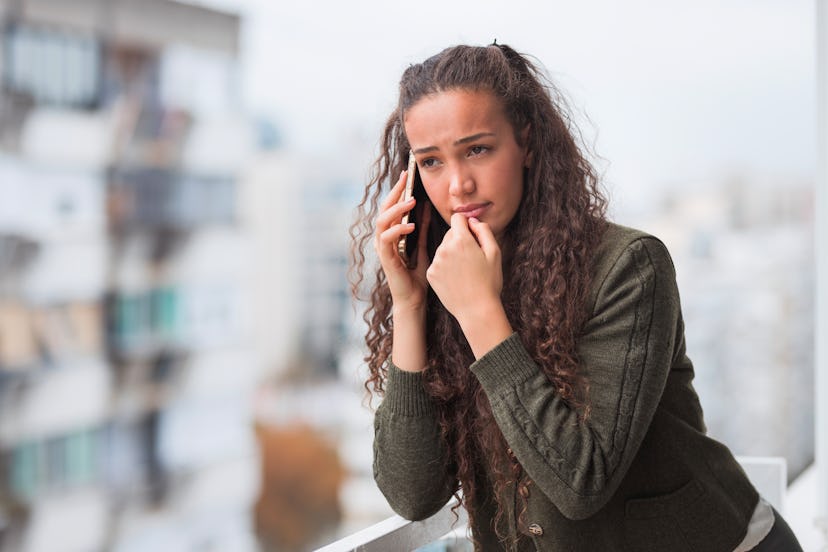 Sad young business woman talking over a phone on a office balcony