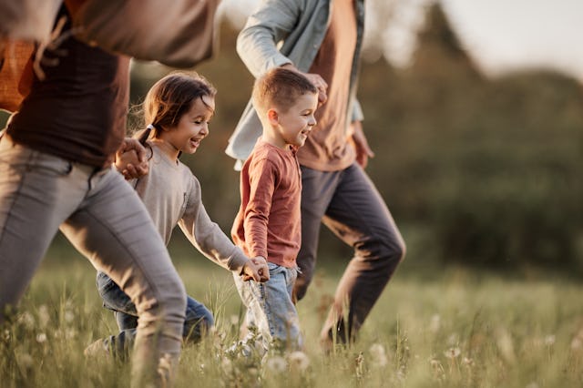 Happy siblings having fun while holding hands with their parents and running during spring day in na...