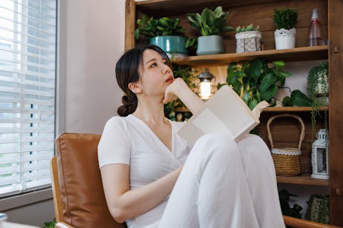 A young and beautiful Asian woman wearing white casual clothing. Sitting on the sofa in the living r...