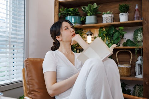 A young and beautiful Asian woman wearing white casual clothing. Sitting on the sofa in the living r...
