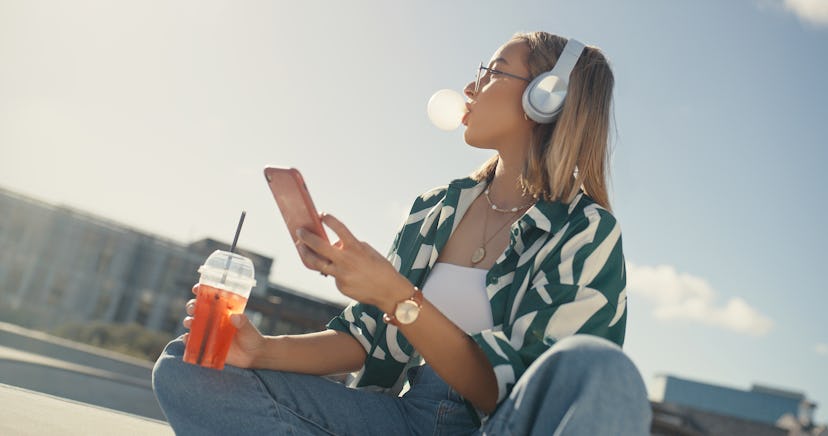 Phone, music and woman with bubblegum in city listening to audio, radio and track in urban park. Fas...