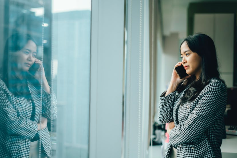 asian businesswoman looking through window talking by phone