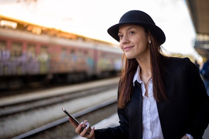 Attractive woman using phone to check train timetable. He waits for the train on the platform and lo...