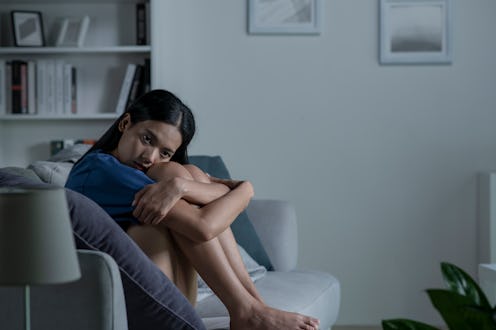 Young Asian woman sitting on sofa at home feeling sad tired and worried suffering depression in ment...