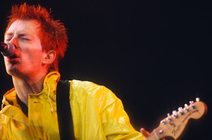 Thom Yorke from Radiohead, wearing a yellow jacket, signing, while playing the guitar.