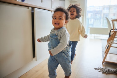 Cute little baby boy and his older brother running through their family kitchen while playing togeth...