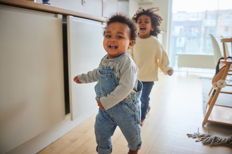 Cute little baby boy and his older brother running through their family kitchen while playing togeth...