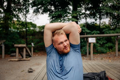 A blonde, white man stretches his arms over his head after exercising outdoors