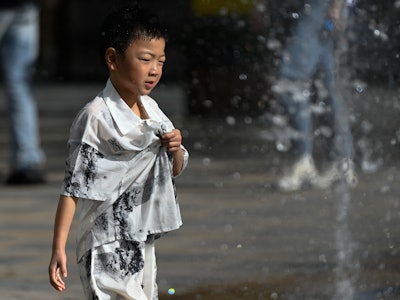 A boy plays among jets of water of a fountain amid hot weather in Beijing on July 5, 2023. (Photo by...