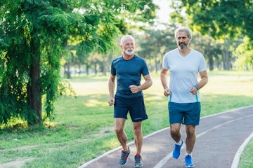 Two senior men jogging outdoors in nature.