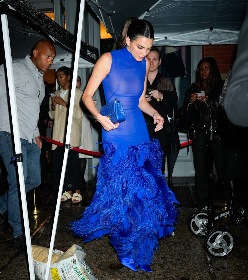 Kendall Jenner wears a cobalt blue sleeveless dress with feathers along the skirt. 
