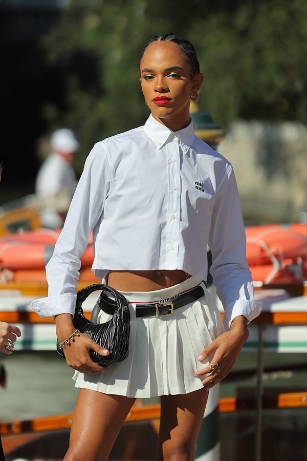 Yasmin Finney wears a white button down, a beige pleated skirt, and a black Miu Miu Wander. 