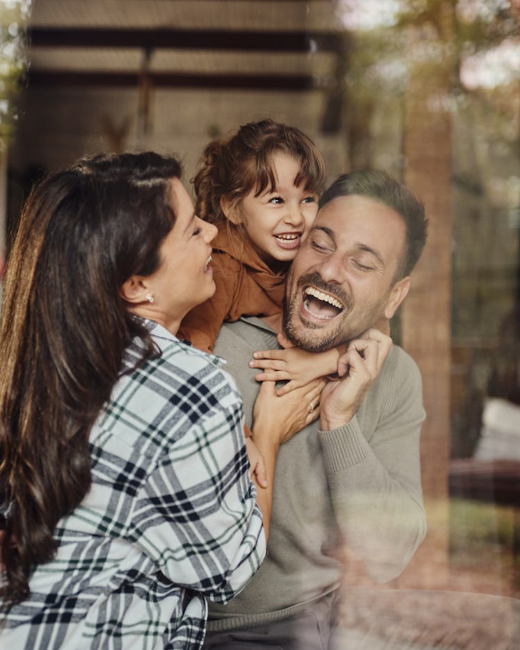 Carefree parents having fun while playing with their small daughter at home. The view is through gla...