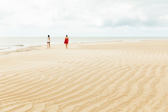 Mother and daughter walking on large strip of sand by low tide in Northeastern Brazil.