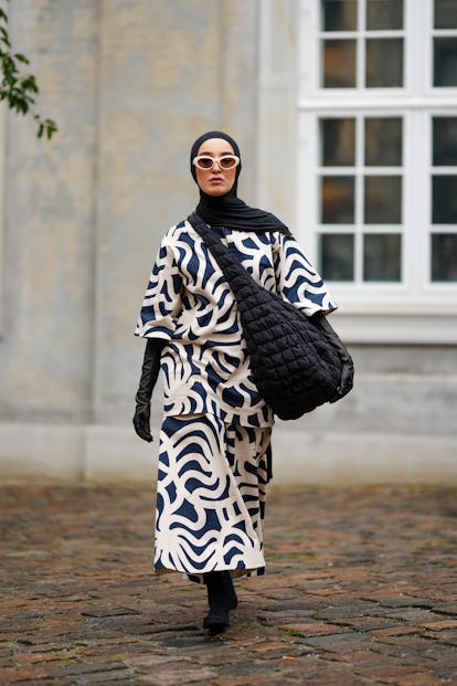 COPENHAGEN, DENMARK - AUGUST 09: A guest wears a black scarf as a headband, white sunglasses, a navy...