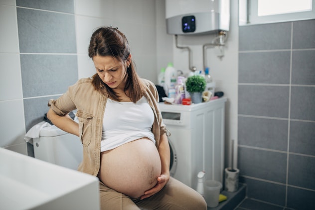 Pregnant woman sitting on toilet seat and having pain in a back, in a story about signs you're dilat...