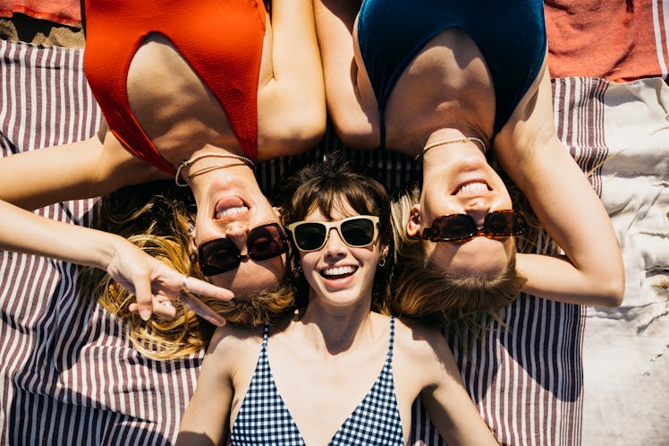 three women pose for an overhead photo as they lay on their beach towel, and consider how the august...