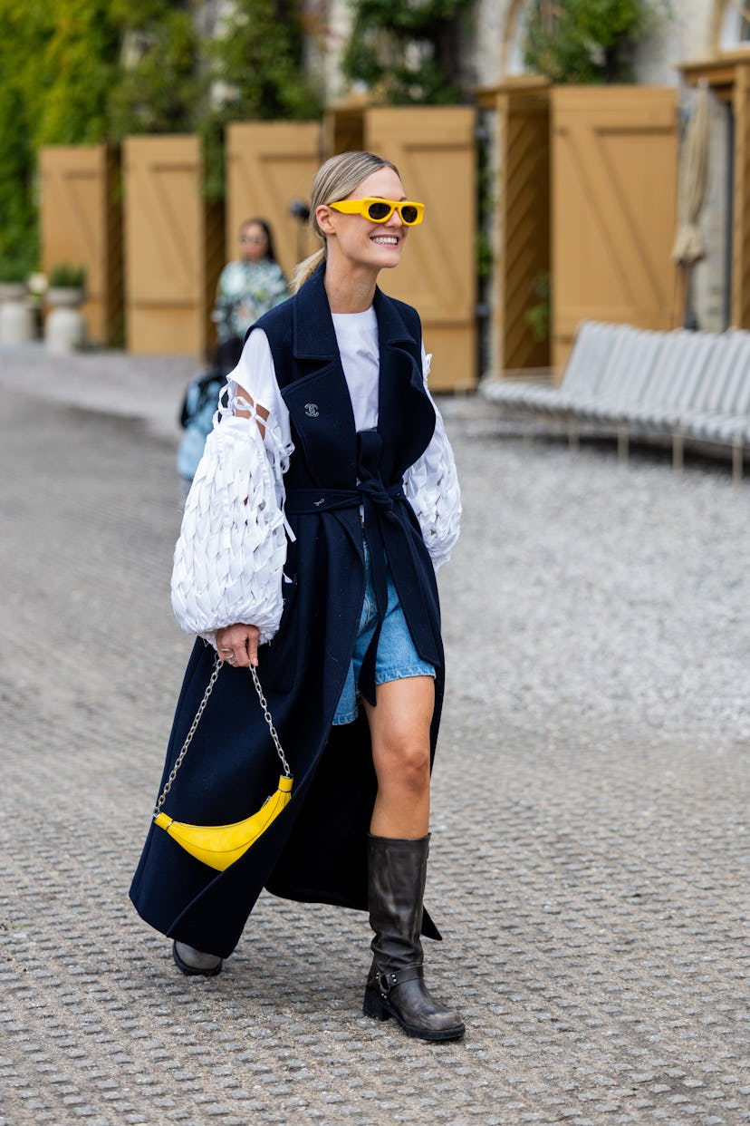 COPENHAGEN, DENMARK - AUGUST 10: A guest wears navy sleeveless coat, white laced top yellow sunglass...