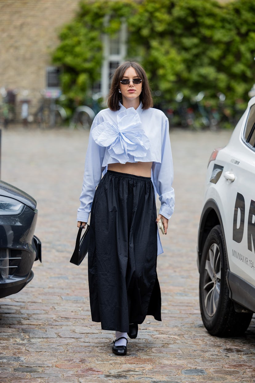 COPENHAGEN, DENMARK - AUGUST 10: A guest wears white cropped shirt with appliquéd flower, black skir...